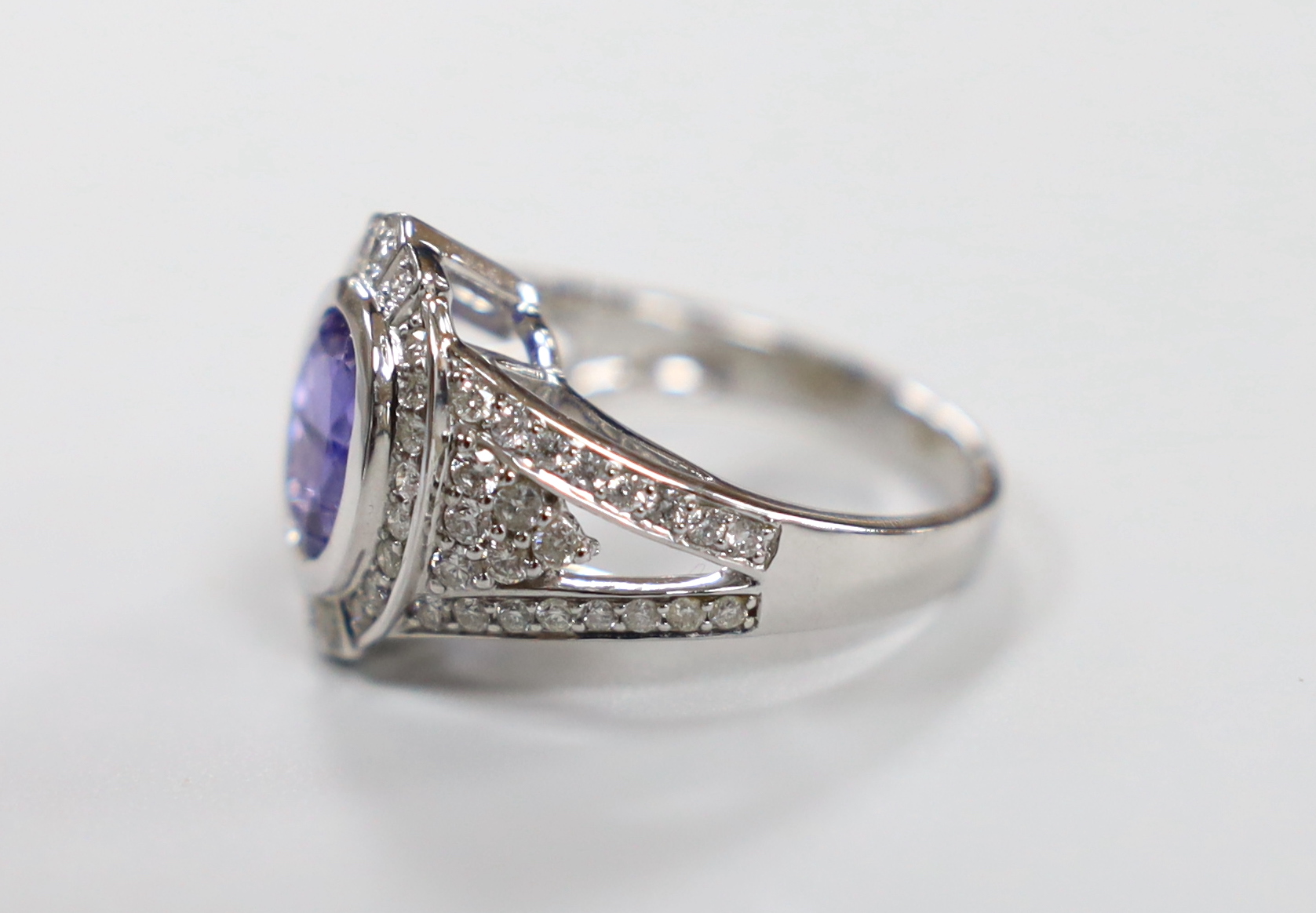 A modern 14k white metal, oval cut tanzanite and diamond chip set cluster dress ring, with diamond chip set shoulders, size M, gross weight 7 grams.